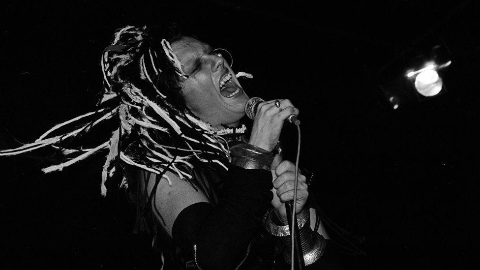 Black and white photograph of Pete Burns on stage singing into microphone 