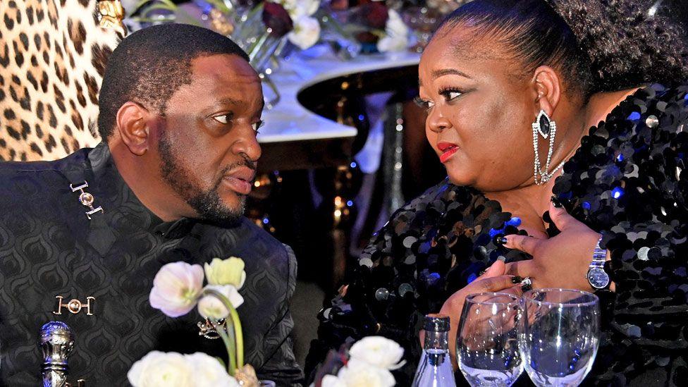 King Misuzulu KaZwelithini and wife Queen Ntokozo kaMayisela look at each other whilst attending a banquet in Johannesburg in 2023. Both are wearing smart black evening dress.