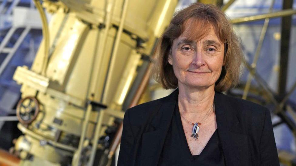 Michele Dougherty in smart black suit standing in front of telescope.