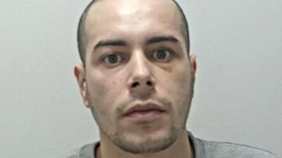 Mohammed Alshafi's mugshot. He has shaved dark hair and stubble and is wearing a grey sweatshirt