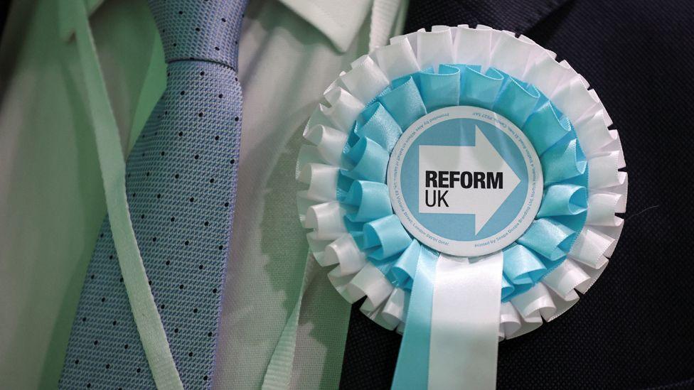  An observer from the Reform UK party wears a rosette