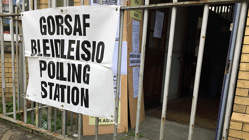 A polling station sign mounted on metal railings outside a community building