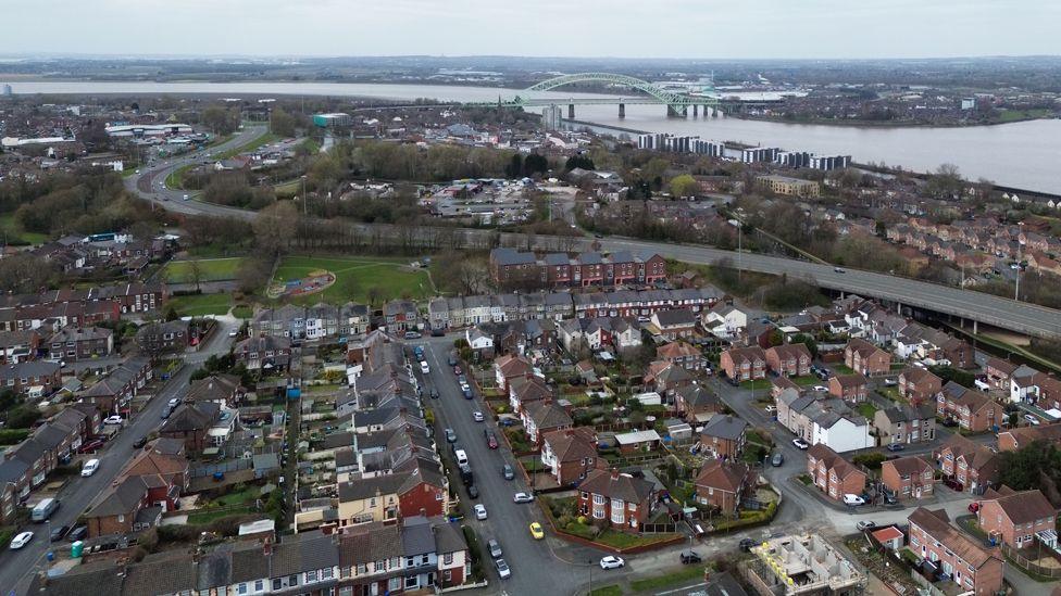 A drone view of Runcorn, showing housing estates in the foreground and the Silvewr Jubilee Bridge over the River Mersey