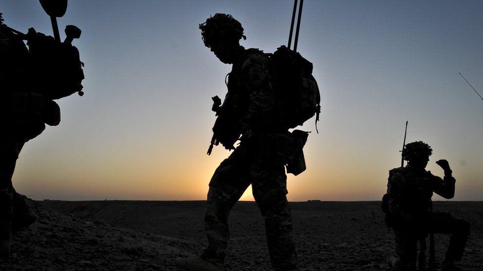 Silhouettes of British soldiers walking against a sunset in Afghanistan