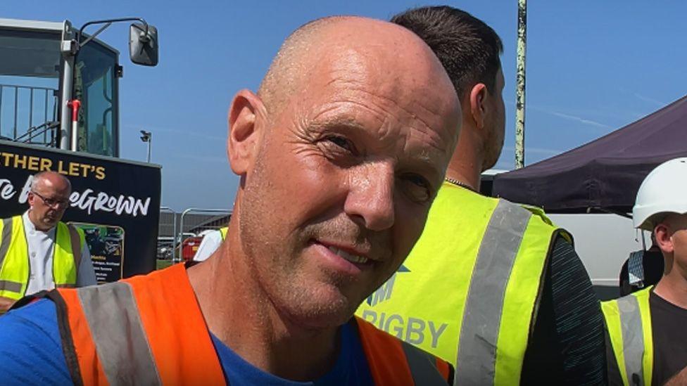 Close up of Ian McDonald in the sunshine wearing a blue t-shirt and orange high vis vest.