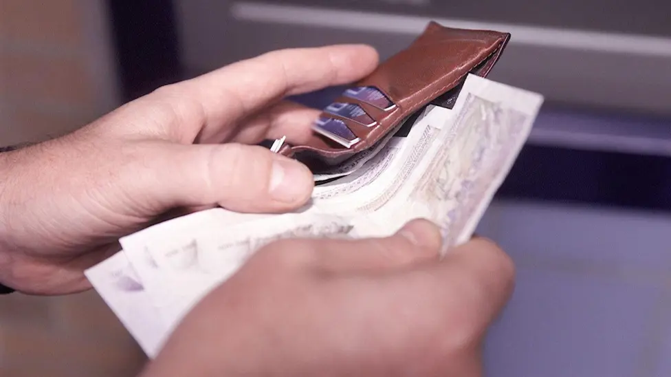 A close-up of hands putting banknotes into a leather wallet