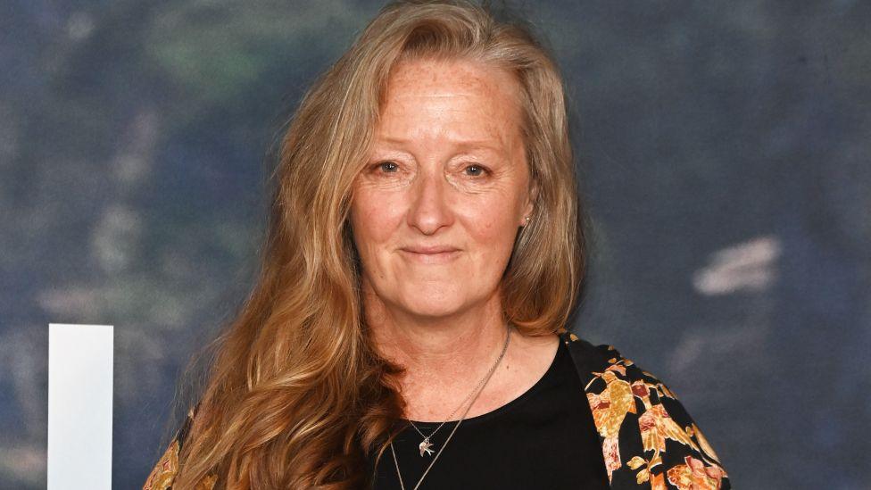 Raynor Winn attends the UK Special Screening of The Salt Path at The Curzon Soho on 22 May 2025 in London. She has long strawberry blonde hair and is wearing a black and yellow top.