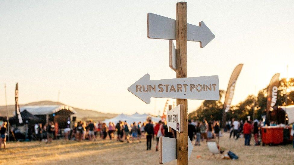 Sign saying Run Start Point in front of a people at a distance in a festival