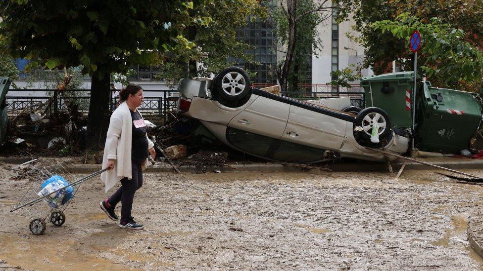 A woman walks with her shopping through muddy streets in Greece following Storm Elias