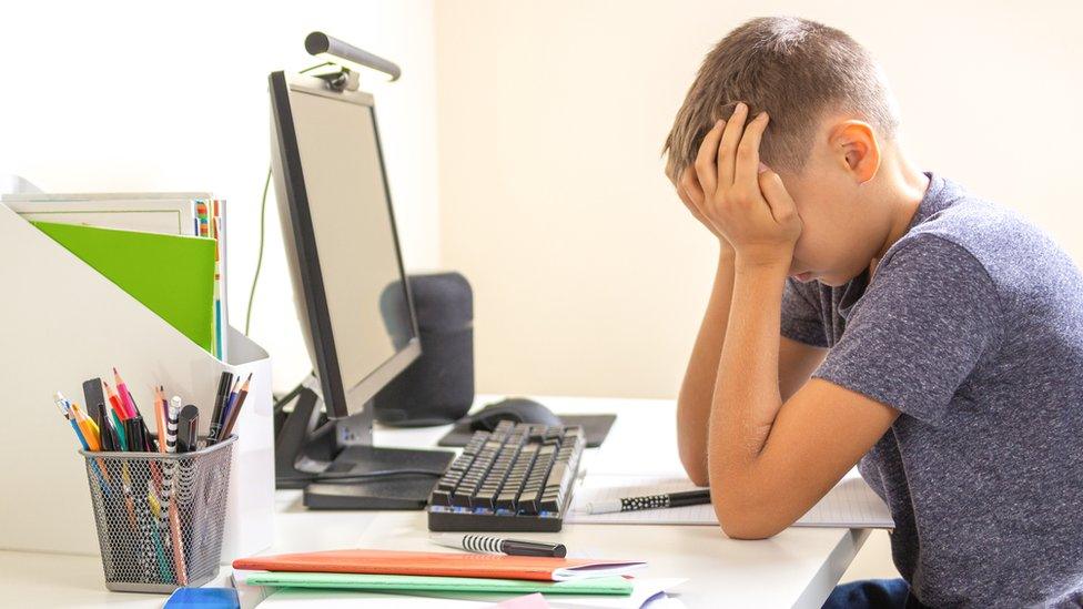 A child sitting at a computer with head in hands