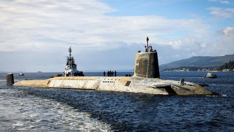 An image of a Vanguard-class submarine half submerged, with people walking along the top