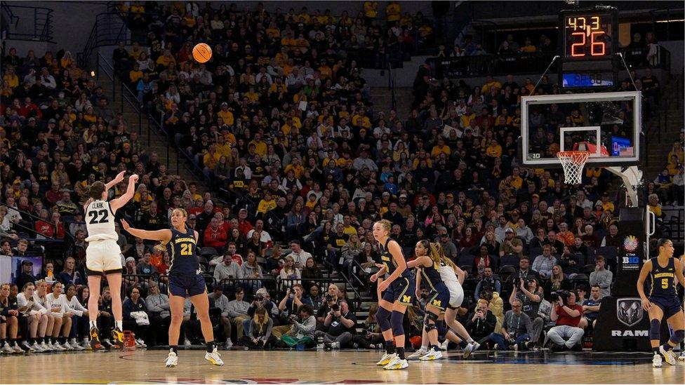 Caitlin Clark jumping, shooting ball in packed stadium