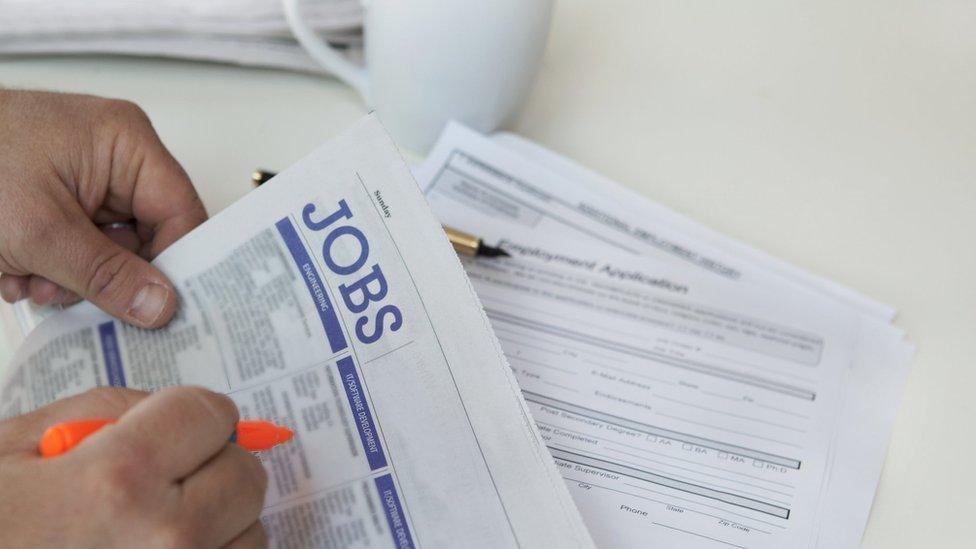 Close-up of hands finding jobs in newspaper with cup in background.