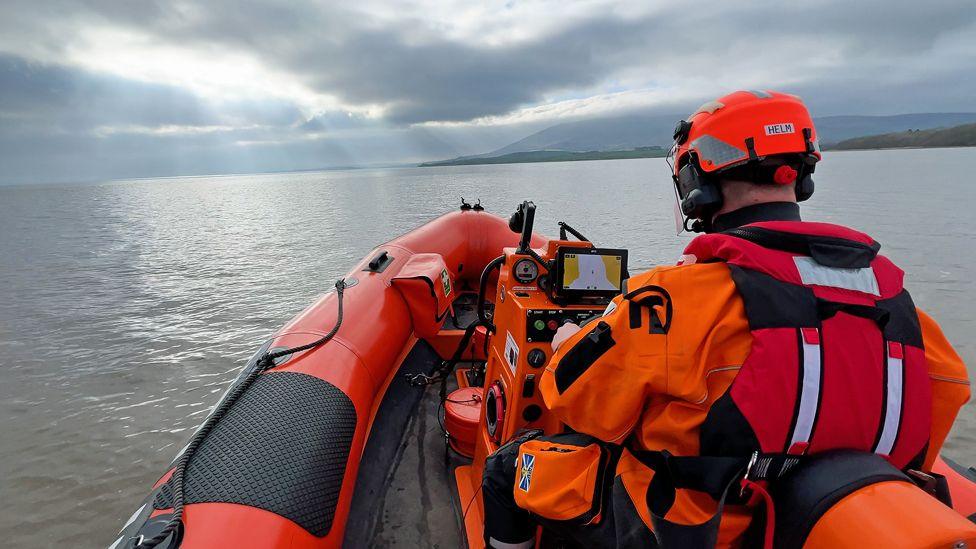 A lifeboat rescuer looks at a computer screen to help navigate across the wide expanse of water in front of him