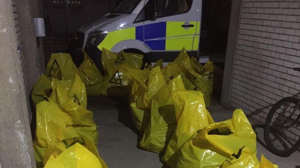 Dozens of bags with biohazard symbols containing what appears to be cannabis in them - a police van can be seen in the background