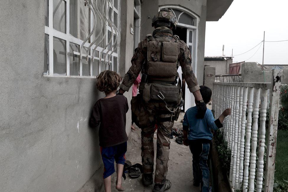 A soldier walks two children into a house in Kukjali