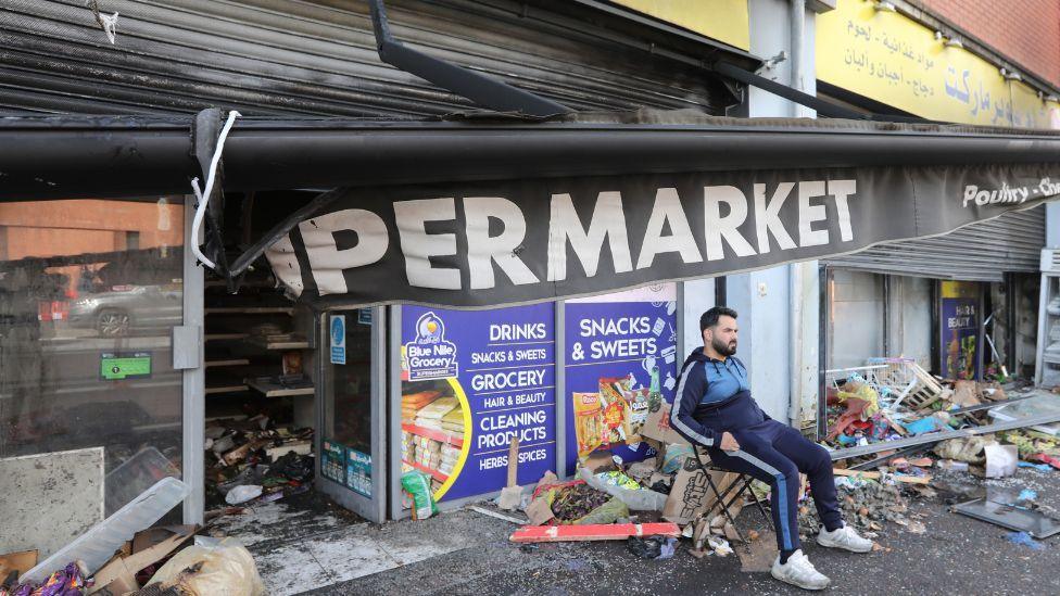 Man sitting outside his burned out shop