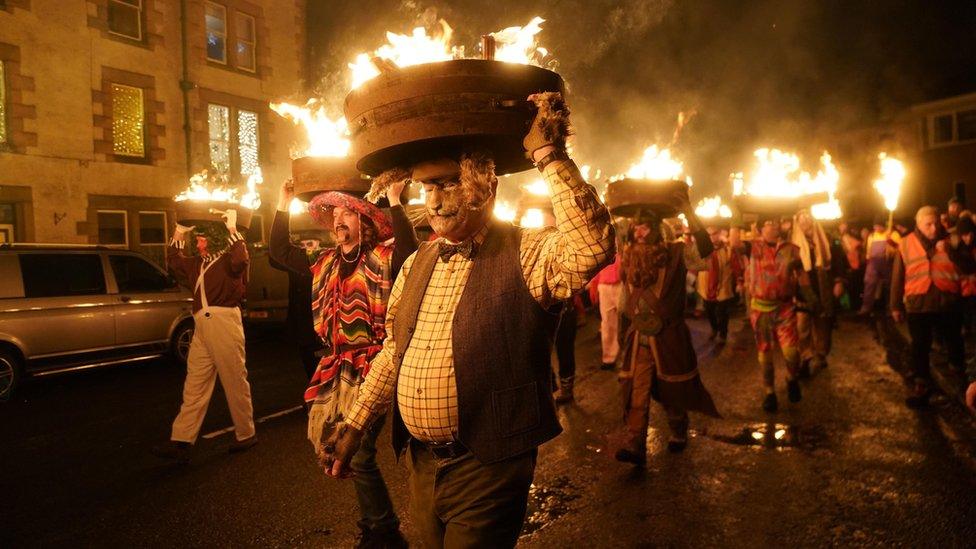 Men, known as guisers, carry burning whisky barrels through the streets during the Allendale