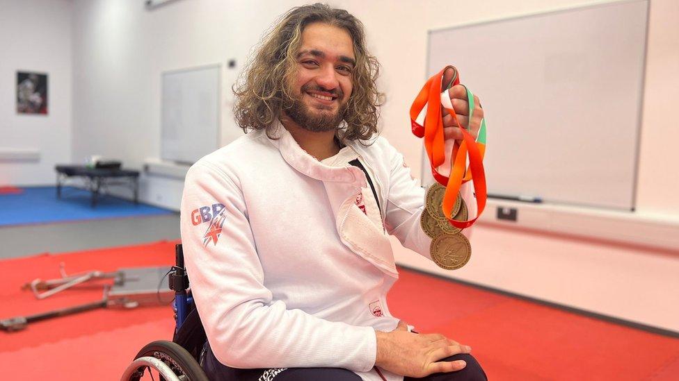 A man in a wheelchair holding gold medals