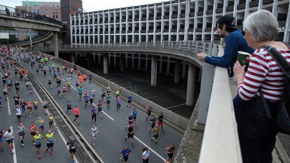 A man and woman stand on a bridge over looking the runners