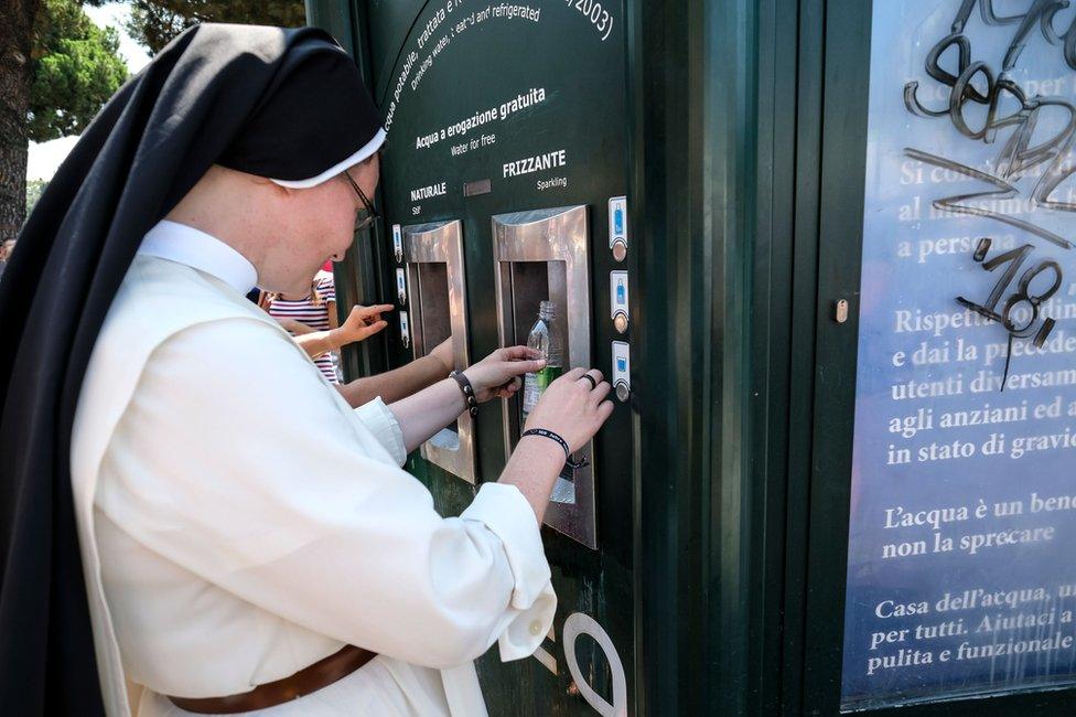 A nun takes water from a kiosk designed in the style of the hexagonal newspaper stands in front of the Ancient Colosseum, in central Rome