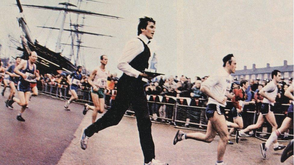 Roger Bourban wearing a waiter's suit and carrying a tray as he runs the London Marathon