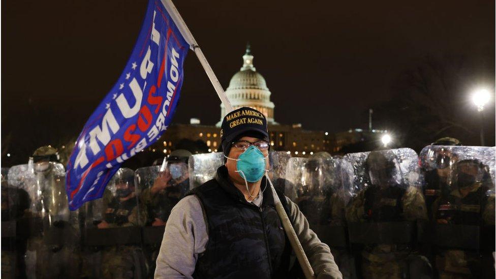 A man in a Trump hat holds a Trump flag outside the US Capitol hours after a riot was declared