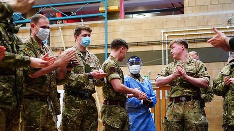 Military personnel stand over medical equipment on the ground as trainers talk them through how to use it.