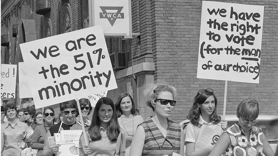 Pro-ERA marchers holding signs saying 'We are the 51% minority' and 'We have the right to vote (for the man of our choice)'