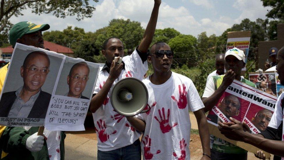 Members of the Rwanda National Congress opposition party shout slogans while holding pictures of slain party founder Patrick Karegeya (L) and posters of Rwandan President Paul Kagame (R) reading 'wanted war criminal' during a demonstration outside the Rwandan embassy in Pretoria on January 9, 2014.