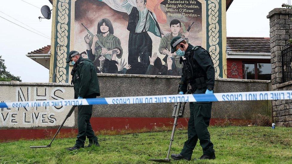 Police officers search the scene in west Belfast where a man was shot three times in his legs