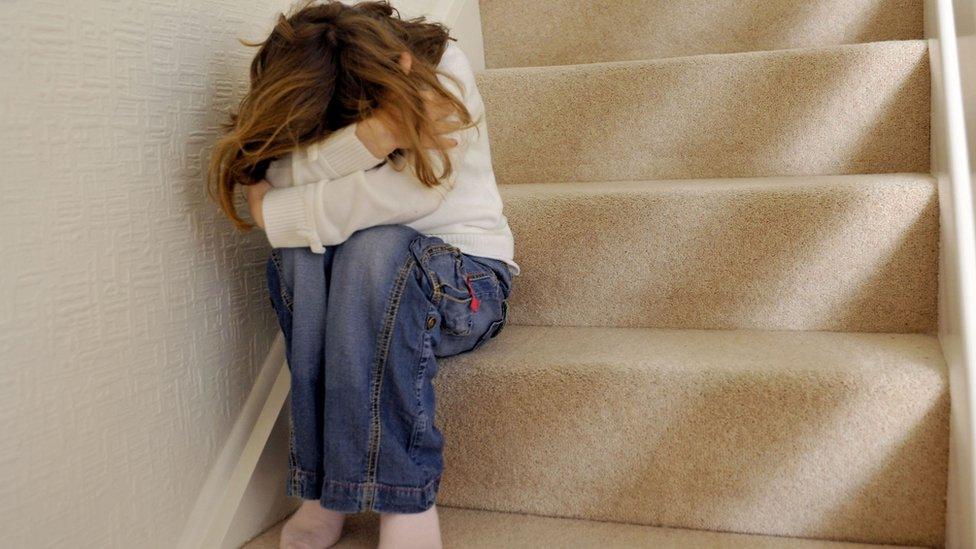 Young girl (6 years of age) sits on the landing of a staircase and covers her face