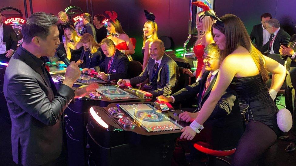 Women dressed as Playboy bunnies watch people use gambling machines