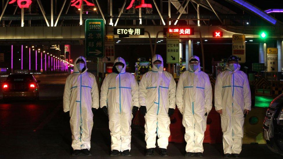 Police wearing protective suits block a road in Shijiazhuang