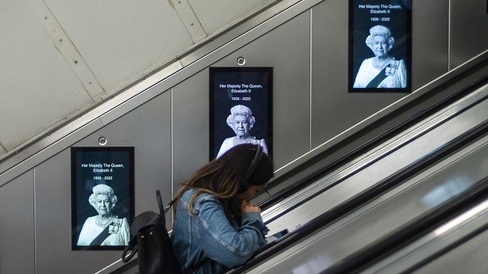 Woman on tube with images of the Queen behind her