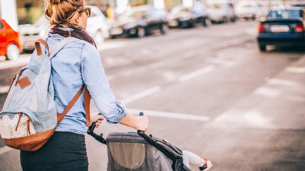 Parent pushing a pram along a road