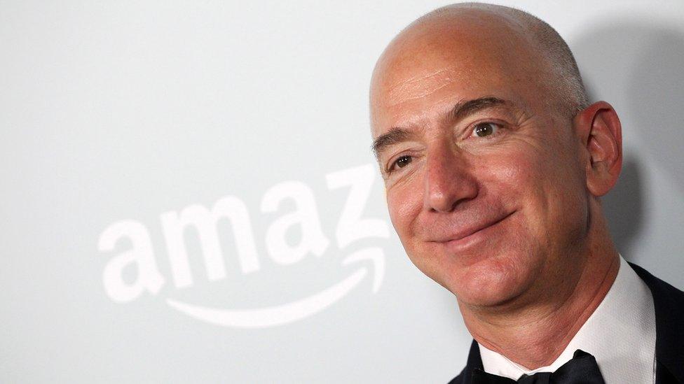 Jeff Bezos standing in front of an Amazon sign