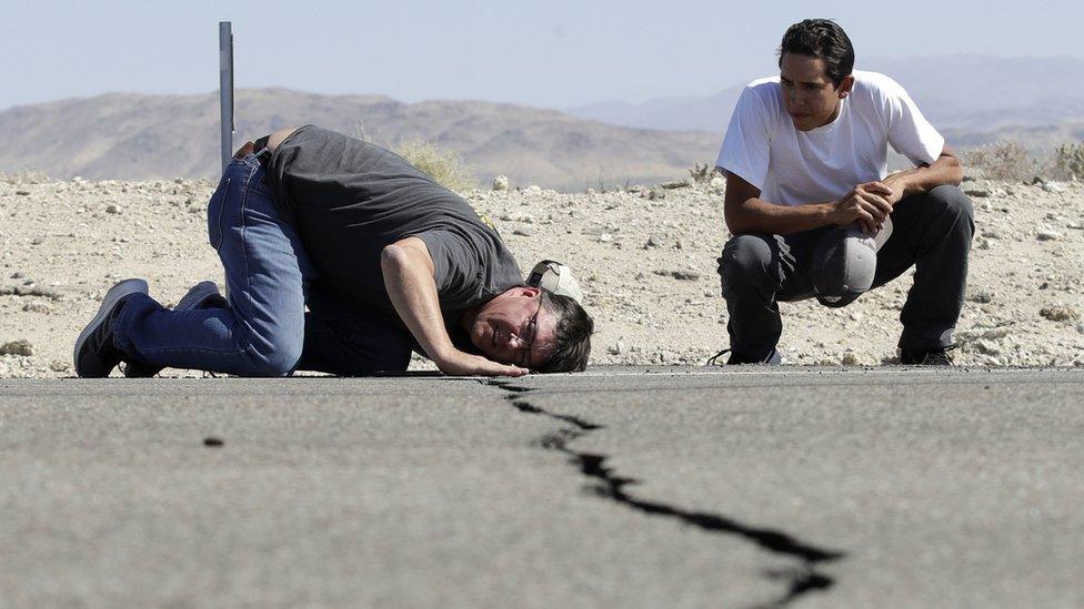 Ron Mikulaco, left, lowers his head to get a look at a crack caused by an earthquake next to his nephew Brad Fernandez on Highway 178 Saturday, July 6, 2019, outside of Ridgecrest, Cali