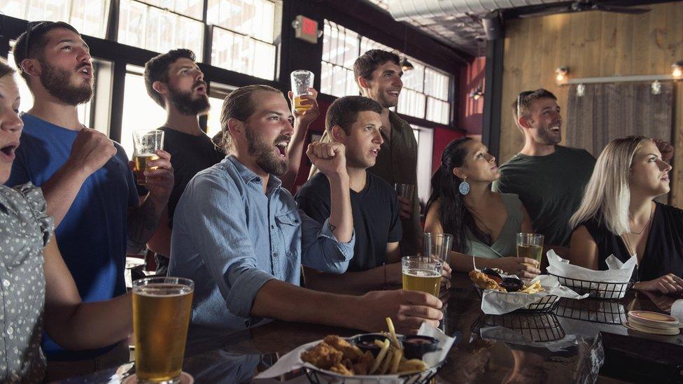 Men and women in a pub watching football on the TV