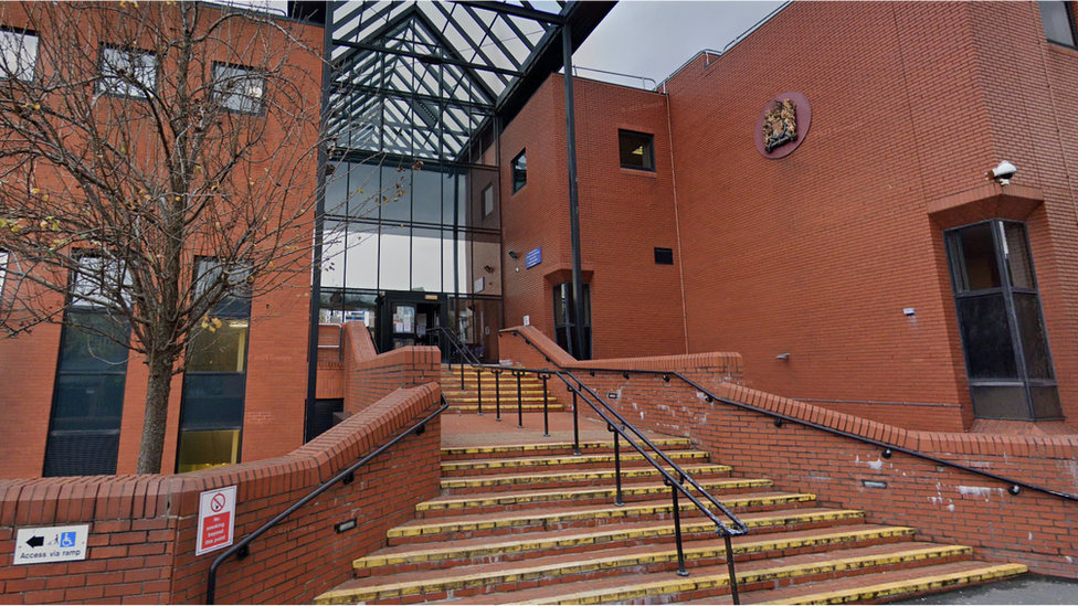 Image of Leicester Crown Court. It is a red brick building with some yellow steps leading up to a glass front entrace.