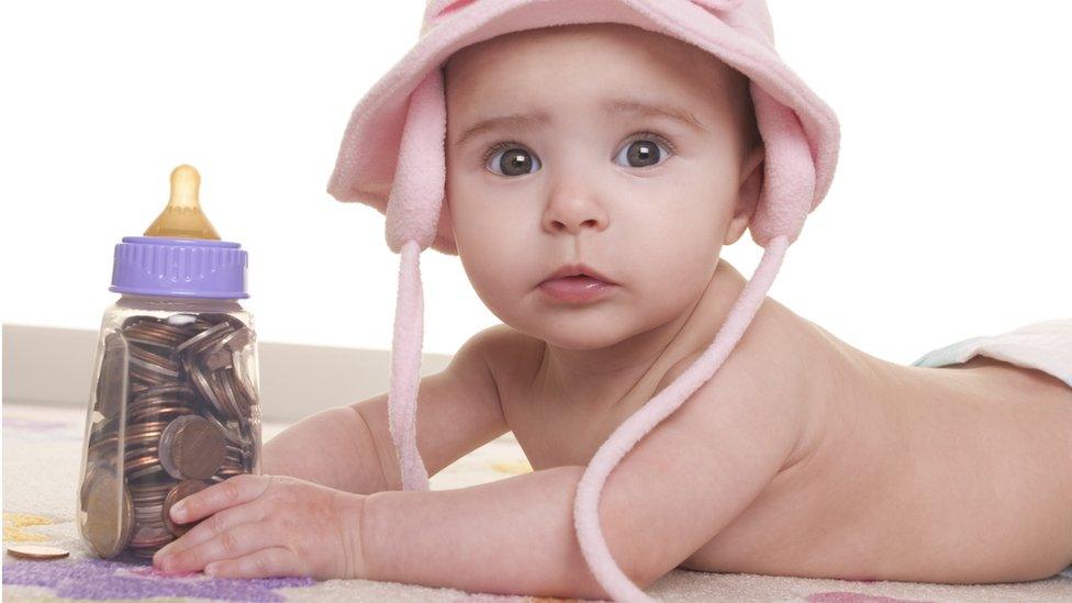 Photo of a baby holding a bottle full of coins