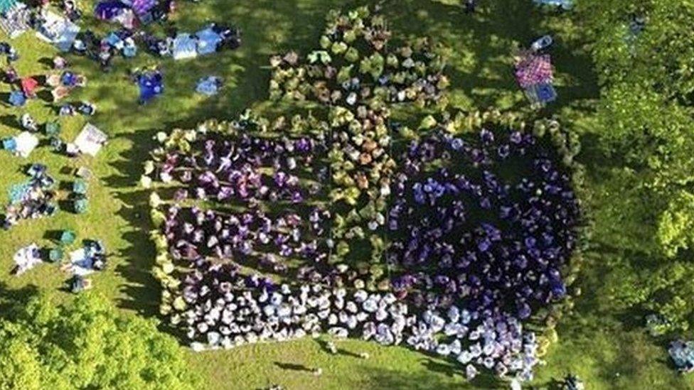 Image of people wearing yellow, purple and white ponchos making up the image of a crown