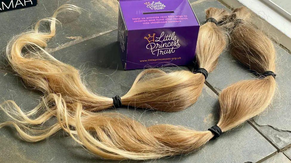 long bits of blond hair tied with black hairbands next to a purple box with the little princess trust logo on it.