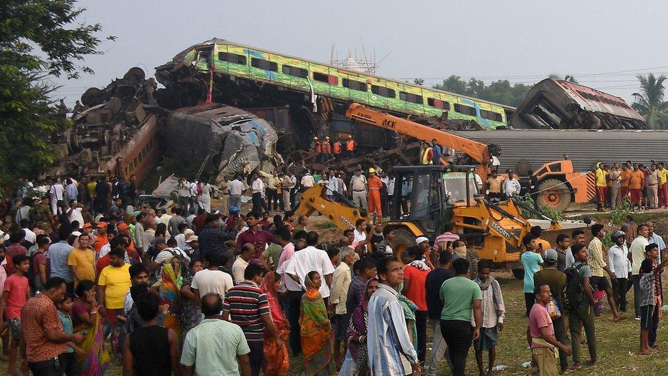 Dozens of people standing next to several severely damaged and overturned train carriages