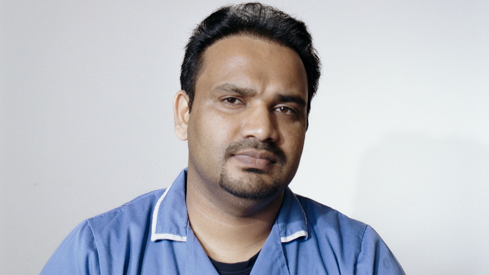 Portrait of Nidheesh Madhava. He has short dark hair and facial hair. He is wearing a blue care uniform with a collar. He is looking directly at the camera with a slight smile.