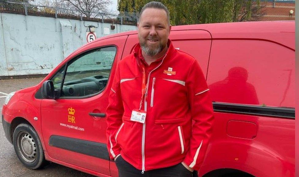 Dan Howells, postman, standing in front of a royal mail van