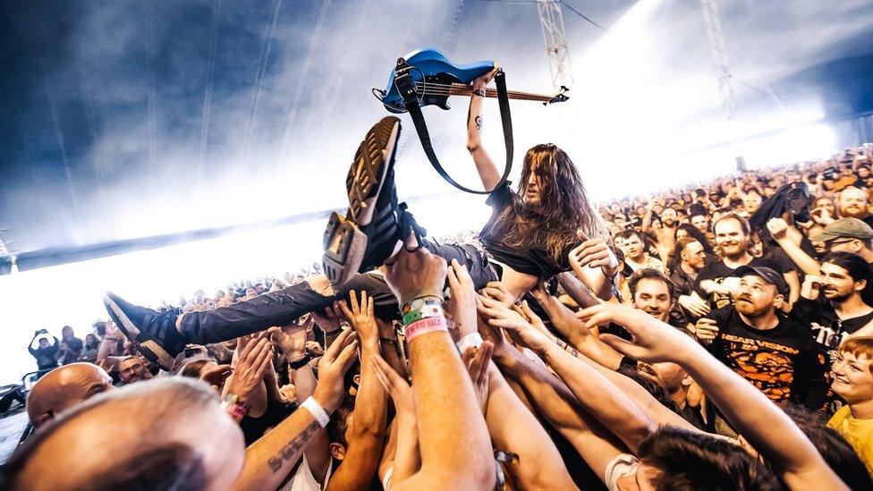 A man crowd-surfing while holding a guitar - he is being held up by lots of hands