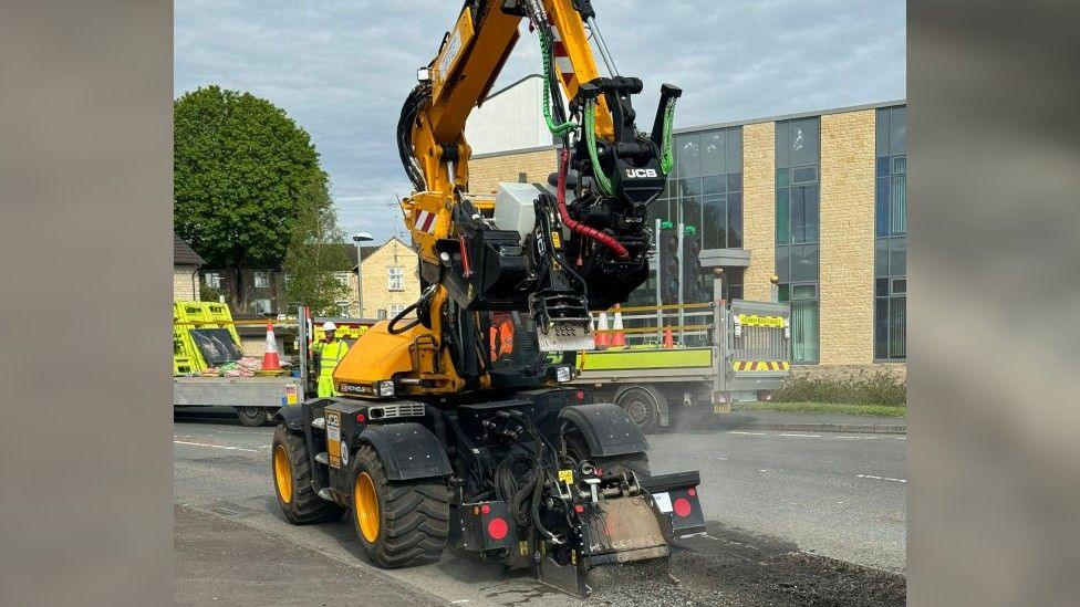 Yellow vehicle with tractor tyres and a pothole filling attachment on an arm