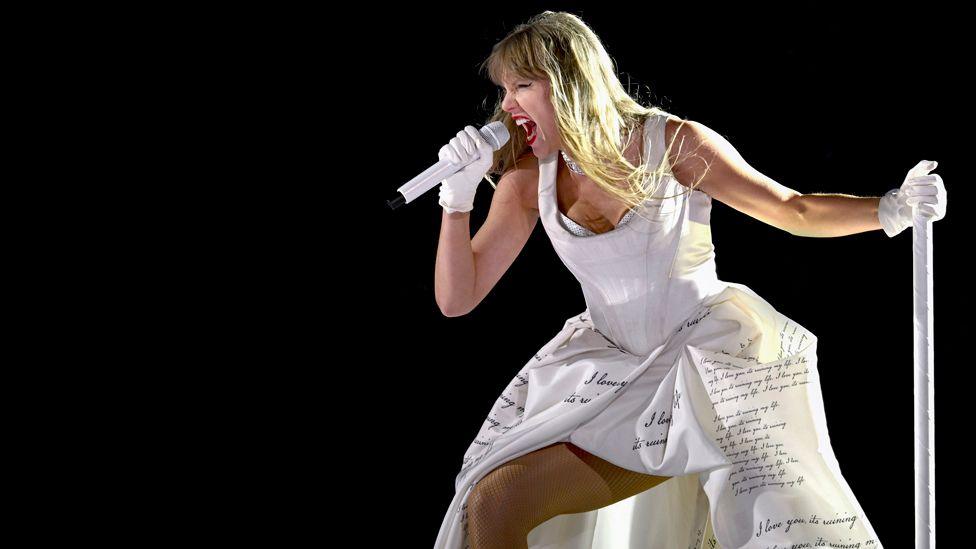 Taylor Swift performing in a white dress covered in lyrics