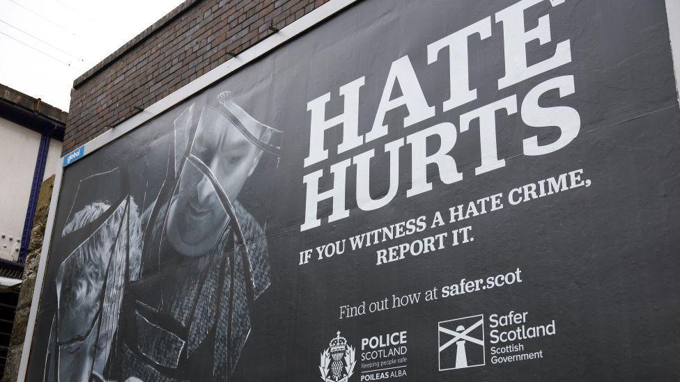 A billboard promoting the Hate Crime and Public Order Act in Scotland, with HATE HURTS written in large white letters on a black background.